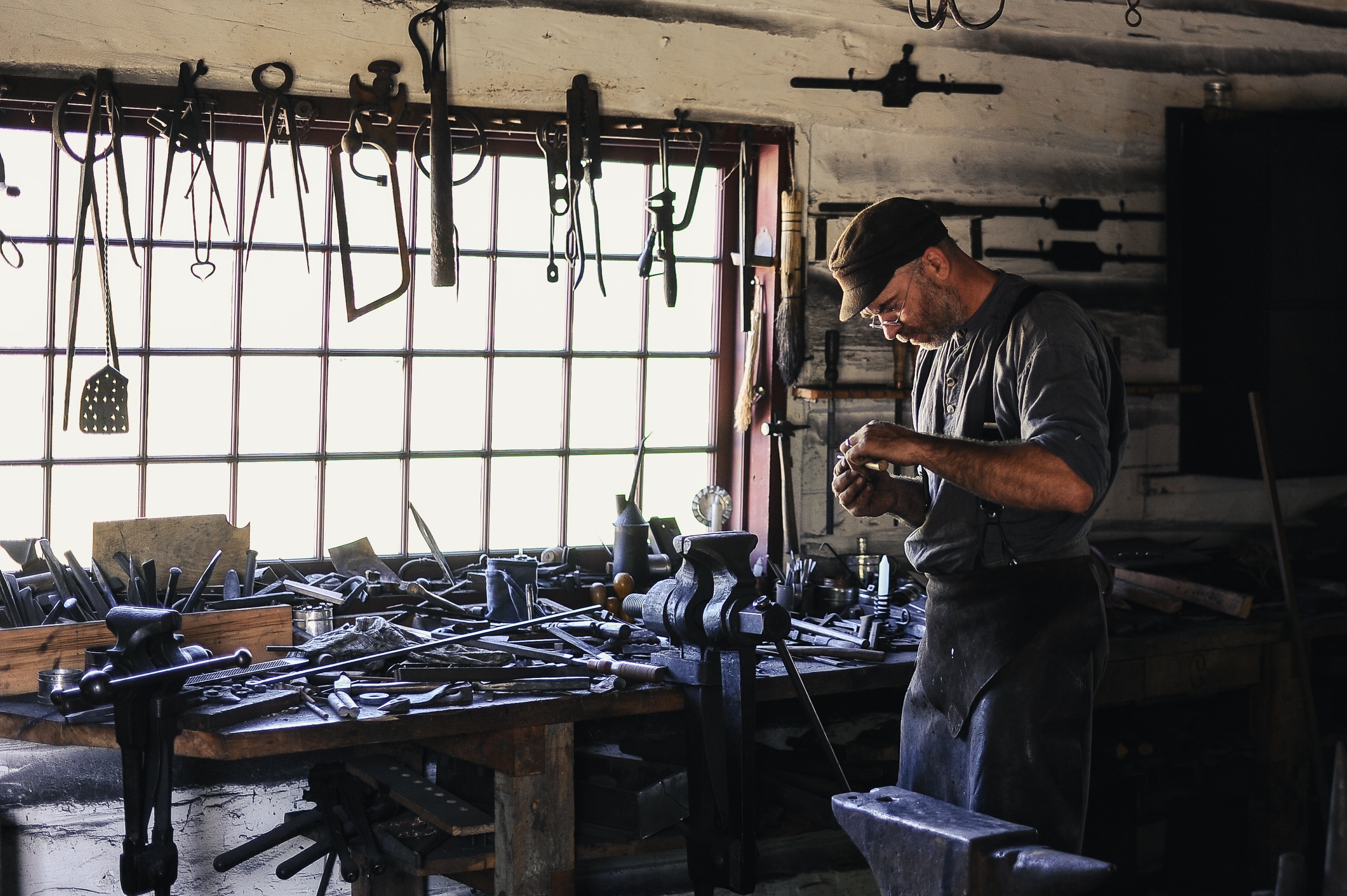 A craftsman working at a workbench covered in metal parts and tools